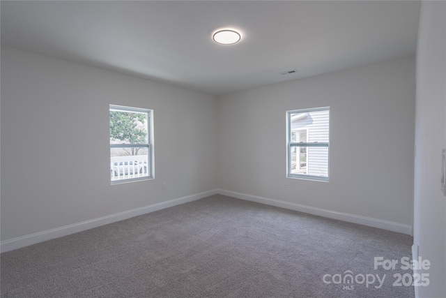 unfurnished room featuring carpet floors, a wealth of natural light, visible vents, and baseboards