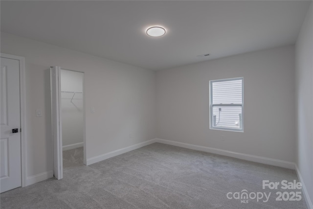 unfurnished bedroom with carpet floors, a spacious closet, and baseboards