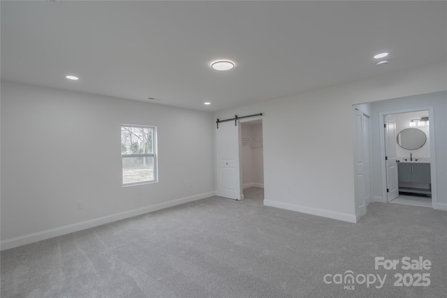 unfurnished bedroom featuring recessed lighting, a barn door, baseboards, and light colored carpet