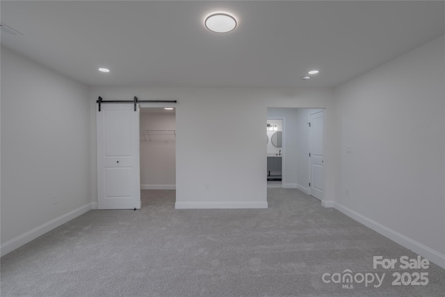 unfurnished bedroom featuring a barn door, recessed lighting, a walk in closet, and baseboards