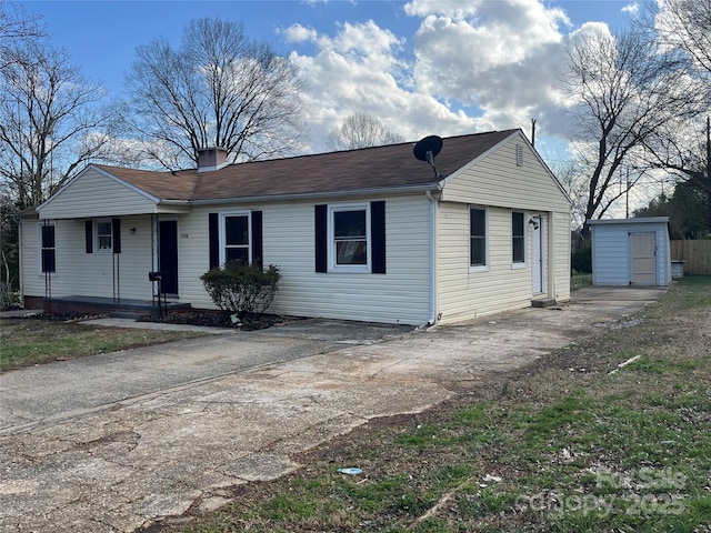 view of front of home featuring concrete driveway, an outdoor structure, a chimney, and a storage shed