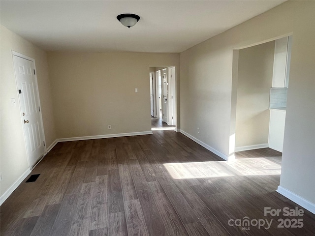 unfurnished room featuring dark wood-type flooring, visible vents, and baseboards