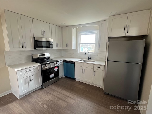 kitchen with stainless steel appliances, decorative backsplash, dark wood-type flooring, white cabinetry, and a sink