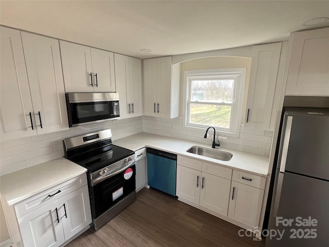 kitchen featuring stainless steel appliances, a sink, white cabinetry, decorative backsplash, and dark wood-style floors