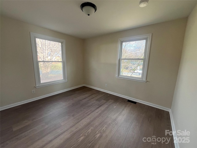 unfurnished room featuring visible vents, dark wood-style floors, a wealth of natural light, and baseboards