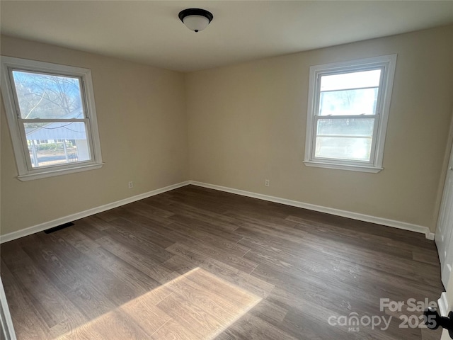 spare room featuring dark wood-style floors, visible vents, and baseboards