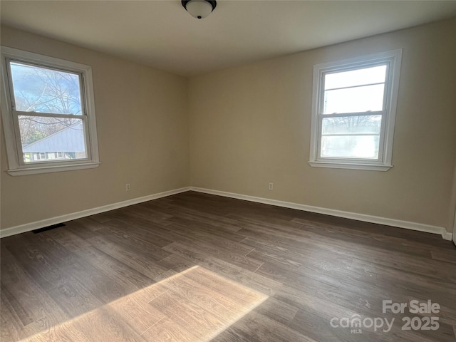 spare room featuring visible vents, dark wood finished floors, a wealth of natural light, and baseboards