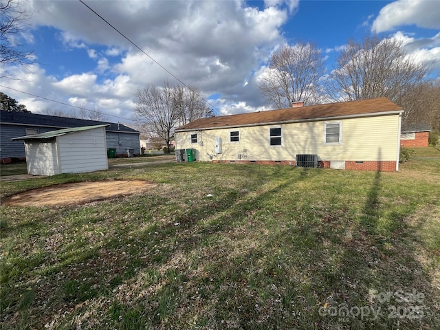 back of house featuring an outbuilding, a chimney, a lawn, crawl space, and central AC