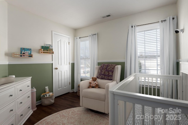 bedroom with a crib, dark wood-style floors, and visible vents