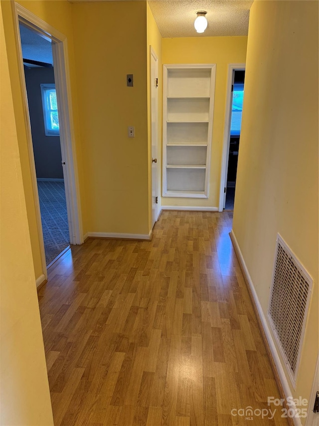 hall with built in shelves, visible vents, a textured ceiling, wood finished floors, and baseboards