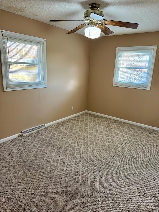 carpeted empty room with a textured ceiling, plenty of natural light, visible vents, and baseboards