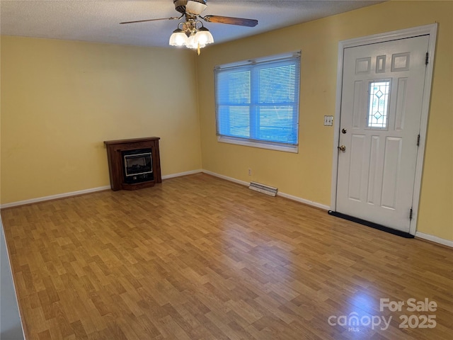 entryway with a fireplace, a ceiling fan, a textured ceiling, wood finished floors, and baseboards