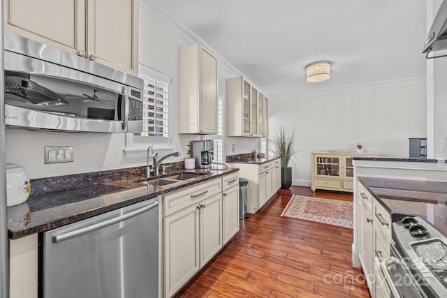 kitchen with crown molding, stainless steel appliances, a sink, dark stone counters, and hardwood / wood-style flooring