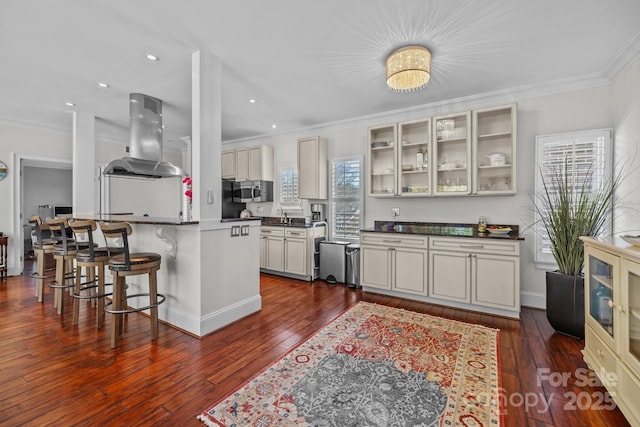 kitchen with dark countertops, dark wood-style flooring, island exhaust hood, and a breakfast bar area