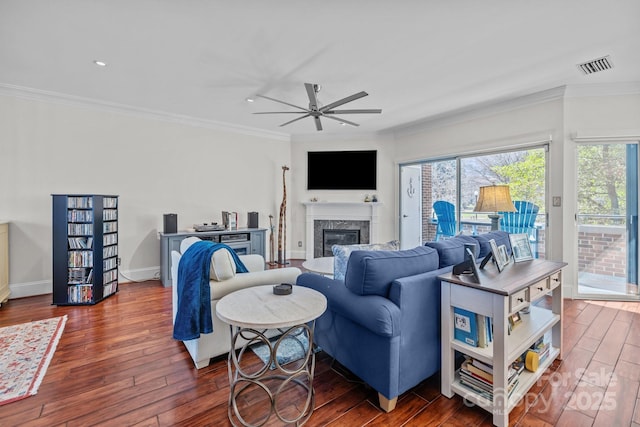 living area with visible vents, hardwood / wood-style flooring, ceiling fan, crown molding, and a high end fireplace