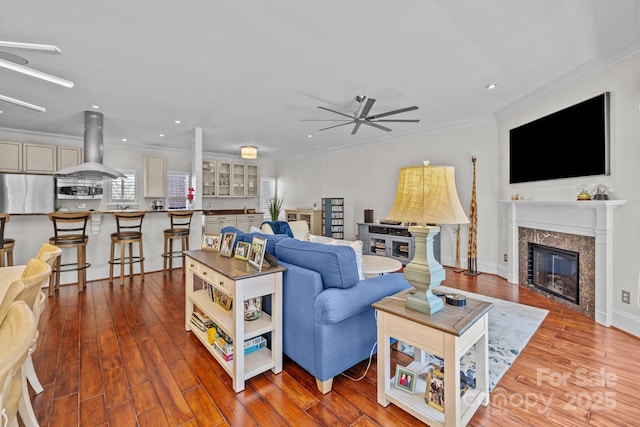 living room featuring wood finished floors, ceiling fan, ornamental molding, and a glass covered fireplace