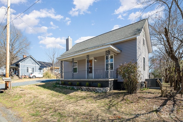 view of front of home featuring roof with shingles, a porch, a chimney, a front lawn, and central air condition unit