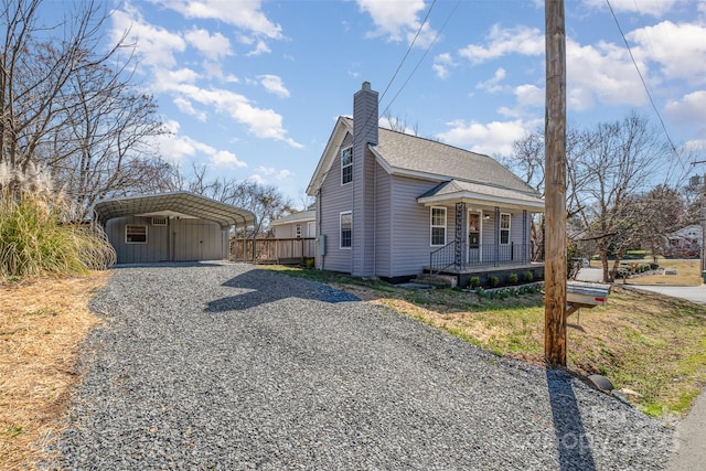 view of side of property with a detached carport, gravel driveway, a porch, roof with shingles, and a chimney