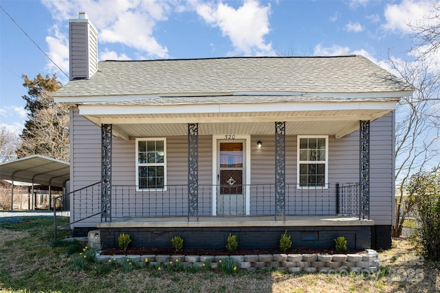 view of front of house with roof with shingles, covered porch, a chimney, a carport, and crawl space