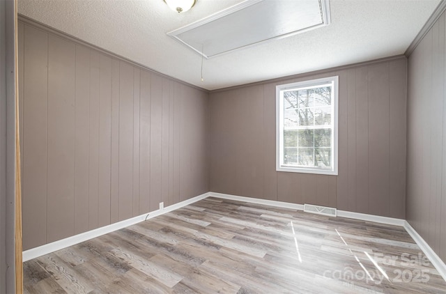 unfurnished room with visible vents, attic access, light wood-style flooring, ornamental molding, and a textured ceiling