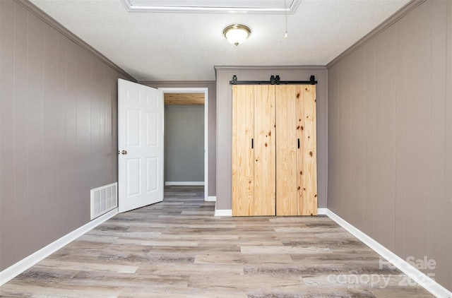 unfurnished bedroom featuring visible vents, ornamental molding, wood finished floors, a barn door, and baseboards