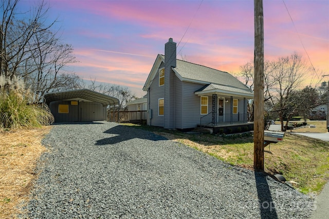 view of front of home with driveway, a porch, a shingled roof, a chimney, and a carport