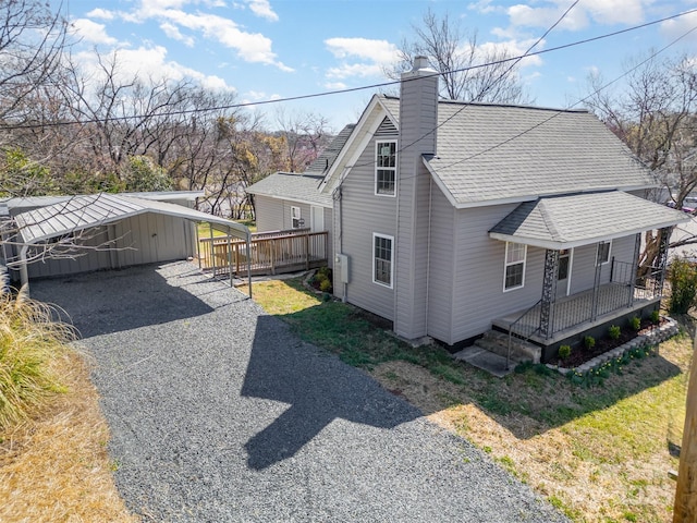 view of side of home featuring driveway, roof with shingles, covered porch, a chimney, and an outdoor structure