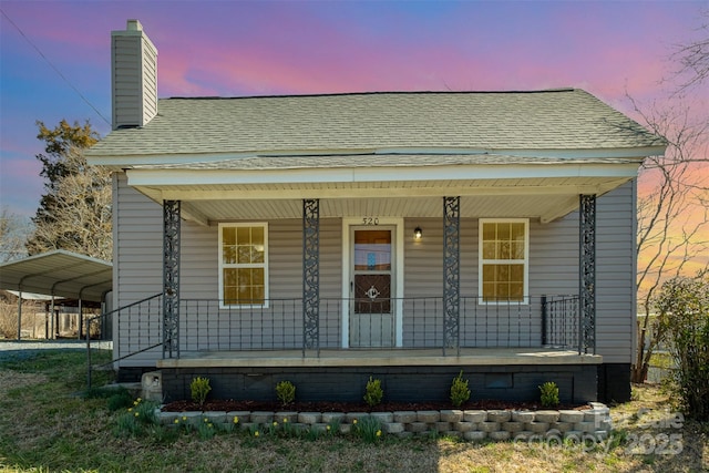 view of front of house featuring a carport, covered porch, a chimney, and roof with shingles