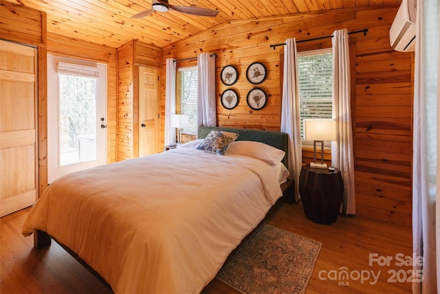 bedroom with a wall unit AC, lofted ceiling, wooden walls, wood finished floors, and wooden ceiling