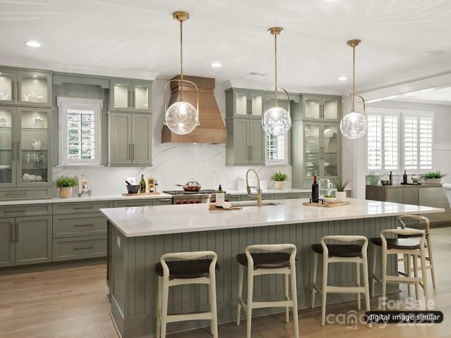 kitchen featuring a sink, custom exhaust hood, a center island with sink, and a healthy amount of sunlight