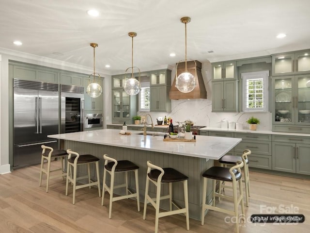 kitchen with green cabinets, appliances with stainless steel finishes, light wood-style floors, a sink, and premium range hood