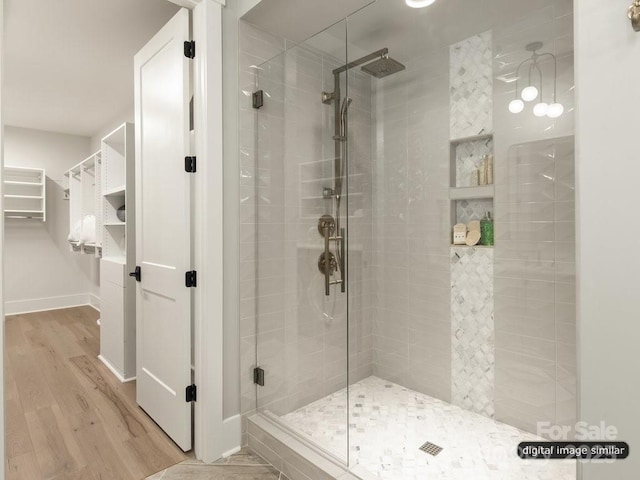 bathroom featuring a spacious closet, a shower stall, baseboards, and wood finished floors