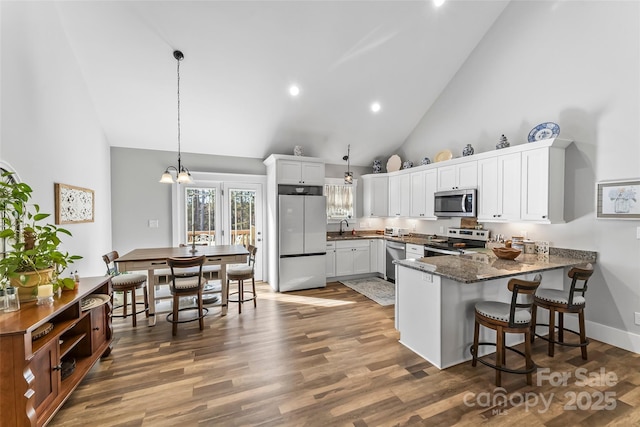 kitchen featuring stainless steel appliances, white cabinetry, a sink, wood finished floors, and a peninsula