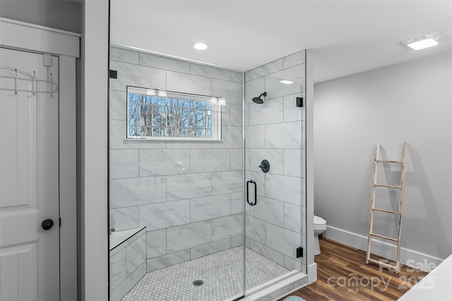 bathroom with a stall shower, wood finished floors, toilet, and baseboards