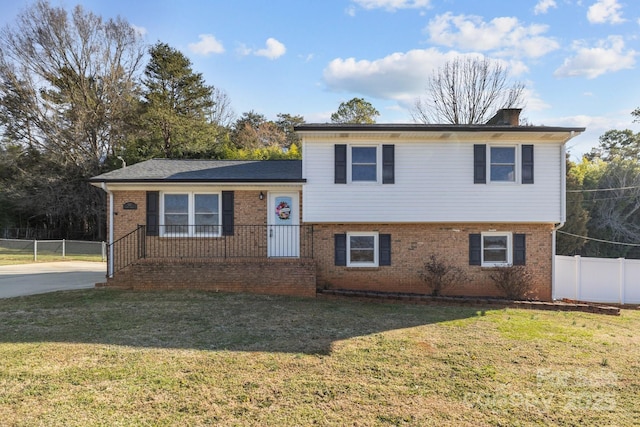 split level home with a chimney, fence, a front lawn, and brick siding