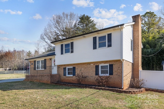 tri-level home featuring a front yard, brick siding, fence, and a chimney