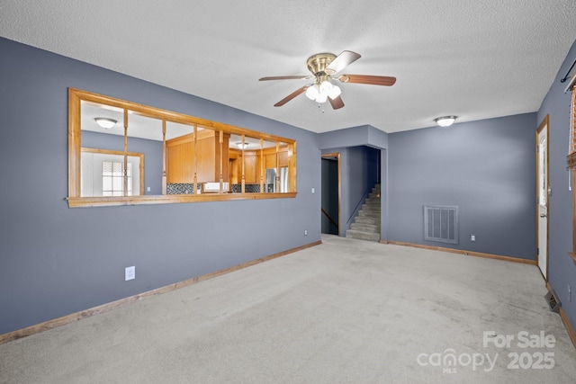 carpeted spare room featuring ceiling fan, stairway, a textured ceiling, and visible vents