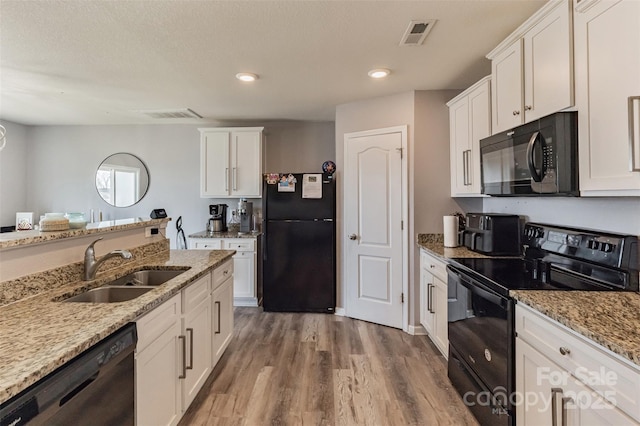 kitchen featuring visible vents, white cabinets, a sink, wood finished floors, and black appliances