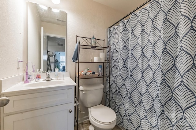 full bath featuring toilet, vanity, visible vents, and a textured wall