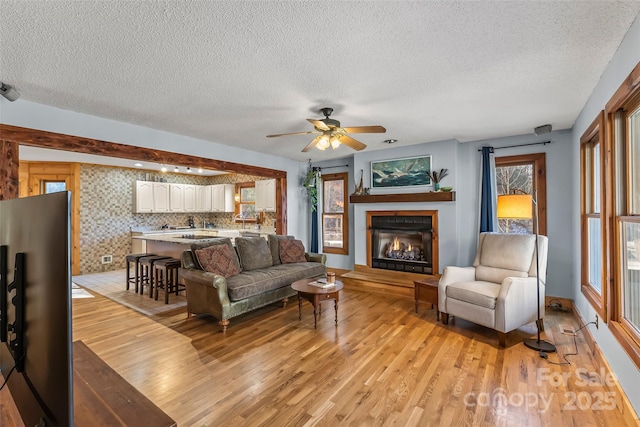 living room with a glass covered fireplace, a textured ceiling, ceiling fan, and light wood finished floors