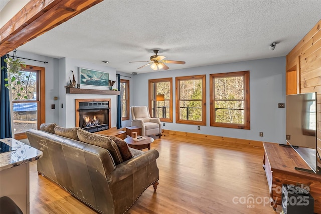 living room with light wood-style floors, a glass covered fireplace, a ceiling fan, and a textured ceiling