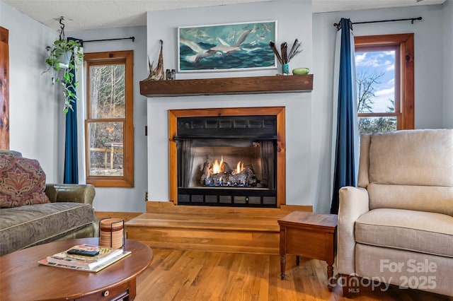 sitting room with wood finished floors, a warm lit fireplace, and a textured ceiling