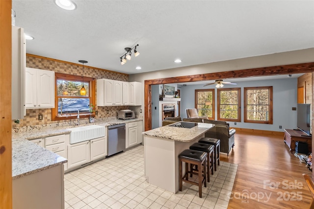 kitchen with a sink, a kitchen bar, stainless steel dishwasher, open floor plan, and a wealth of natural light