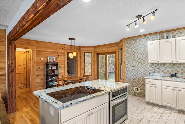 kitchen featuring a kitchen island, oven, black electric stovetop, white cabinets, and a textured ceiling