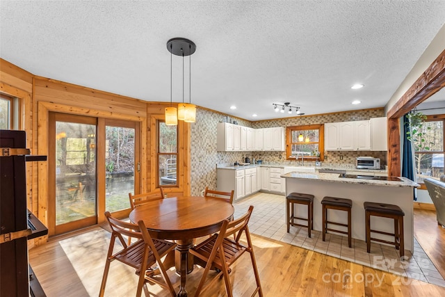 dining space featuring wallpapered walls, a toaster, a textured ceiling, and light wood finished floors