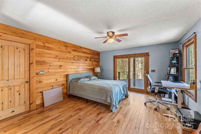 bedroom with light wood-style flooring, a ceiling fan, access to outside, a textured ceiling, and wood walls