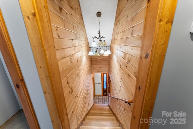 stairs with wooden walls and a notable chandelier