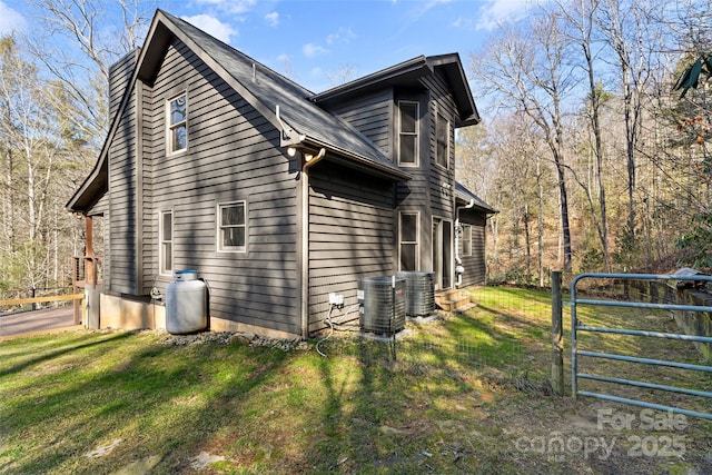 view of side of property featuring a lawn, central AC, and a gate