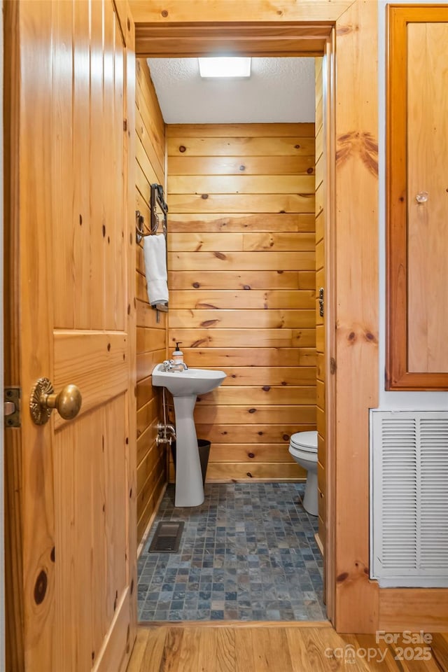 bathroom with toilet, wood finished floors, visible vents, and wood walls