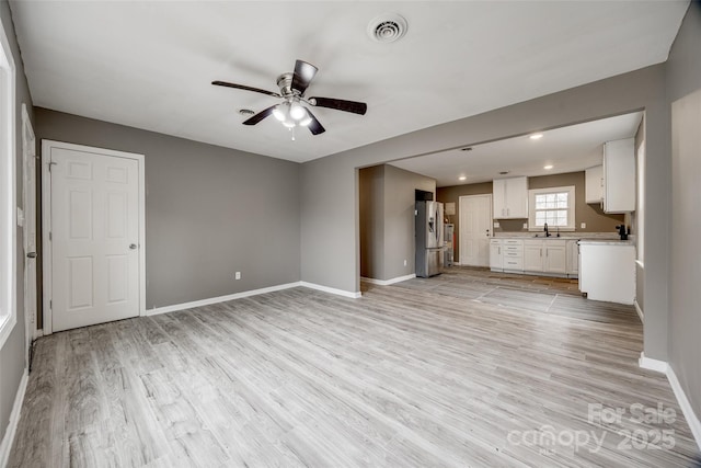 unfurnished living room featuring ceiling fan, a sink, visible vents, baseboards, and light wood-type flooring